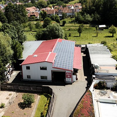 Luftaufnahme eines Gebäudes mit Solarmodulen auf dem Dach, die von einem erfahrenen Dachdecker fachmännisch installiert wurden und von üppigem Grün und anderen Strukturen umgeben sind.